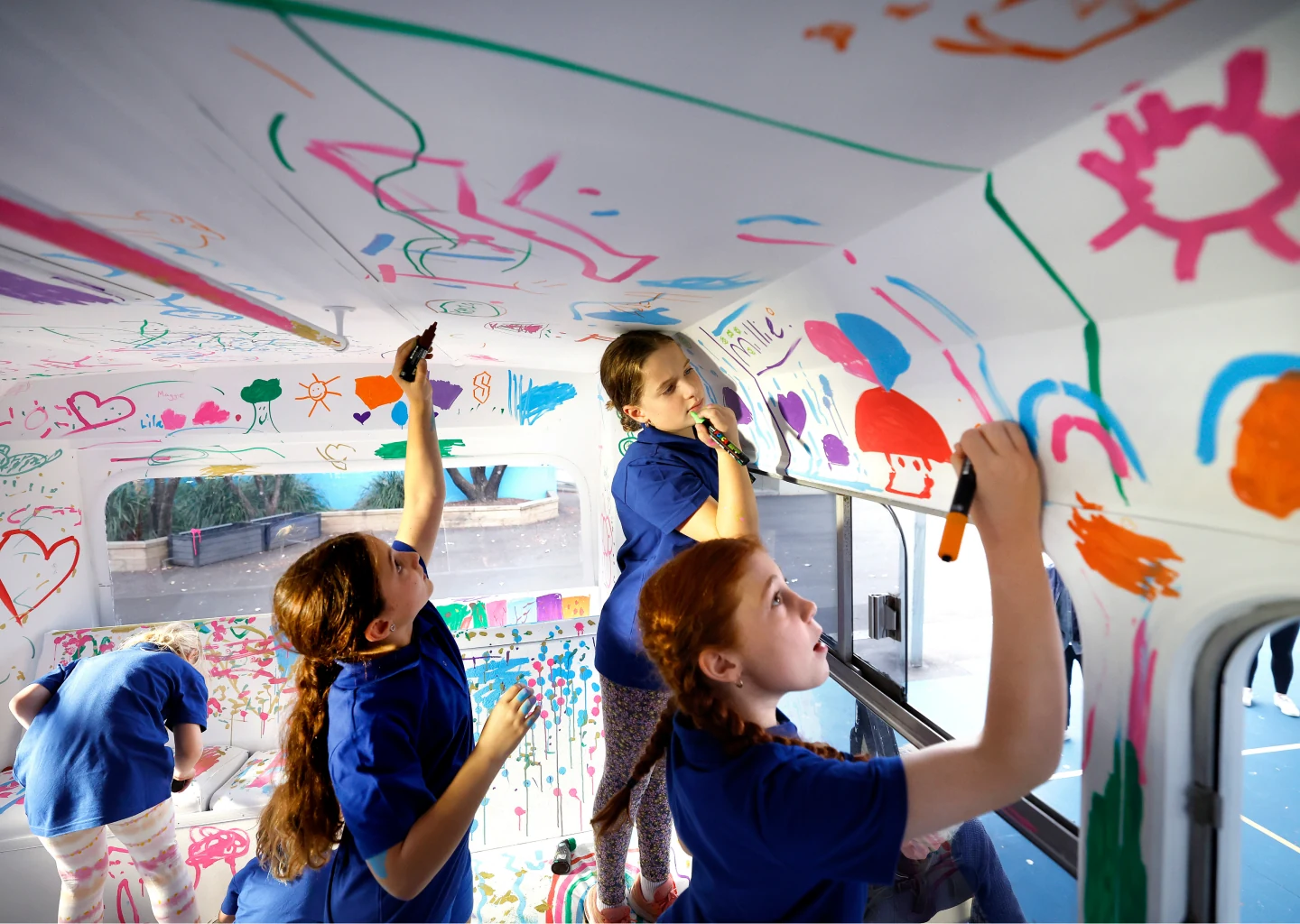 Schoolchildren creating colourful artwork inside a bus.